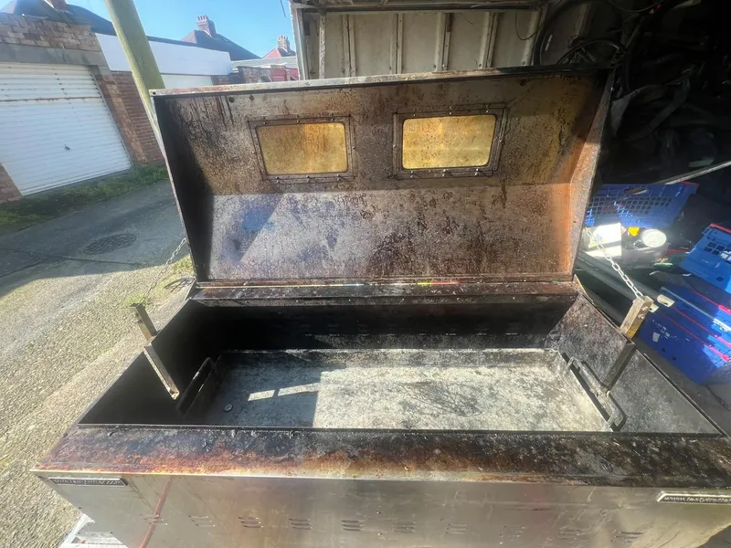 Hog roast machine with its lid open, the inside black with burnt-on grease